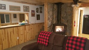 A cozy living room with a stone fireplace, wooden paneling, and a couch with a checkered throw. - Petoskey - Enjoy the great outdoors from the Cozy and peaceful cabin! (Petoskey)