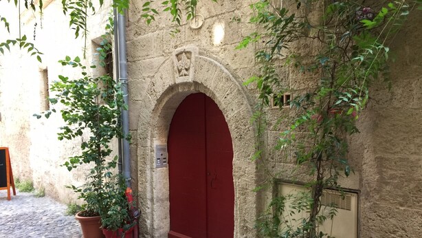 Un bâtiment en pierre avec une porte rouge, des plantes en pot et une rue pavée.