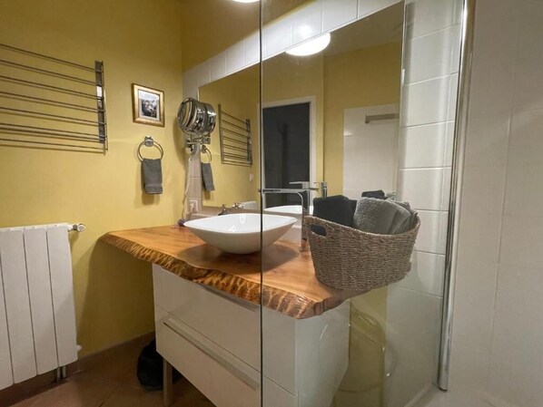 Une salle de bain avec un plan de toilette en bois, un lavabo blanc, un miroir, un porte-serviettes et un panier.