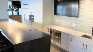 A modern kitchen with a large island, stainless steel appliances, and a flat-screen TV mounted on the wall.
