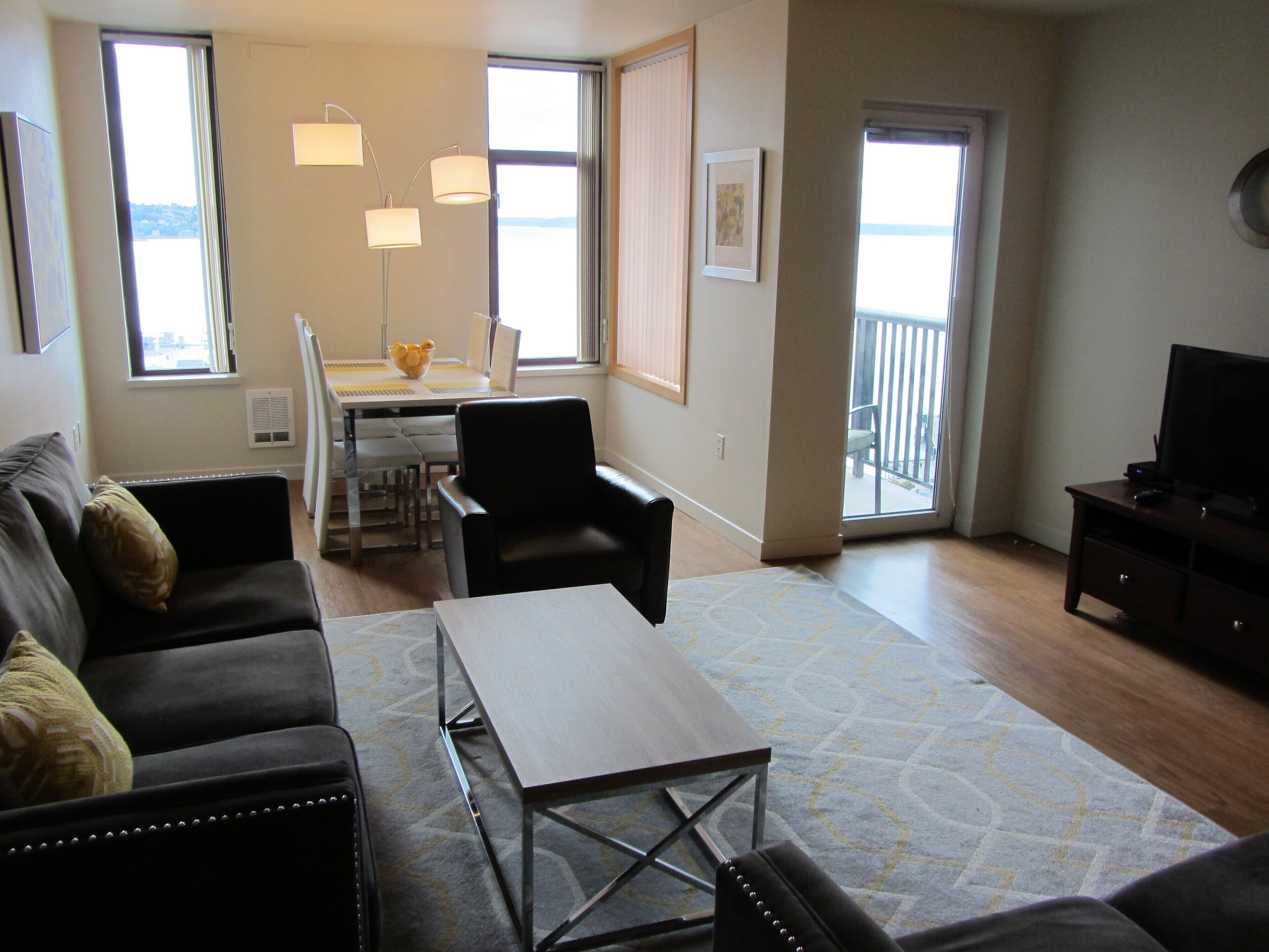 A living room with a sofa, a coffee table, and a TV stand. There is a dining area with a table and chairs.