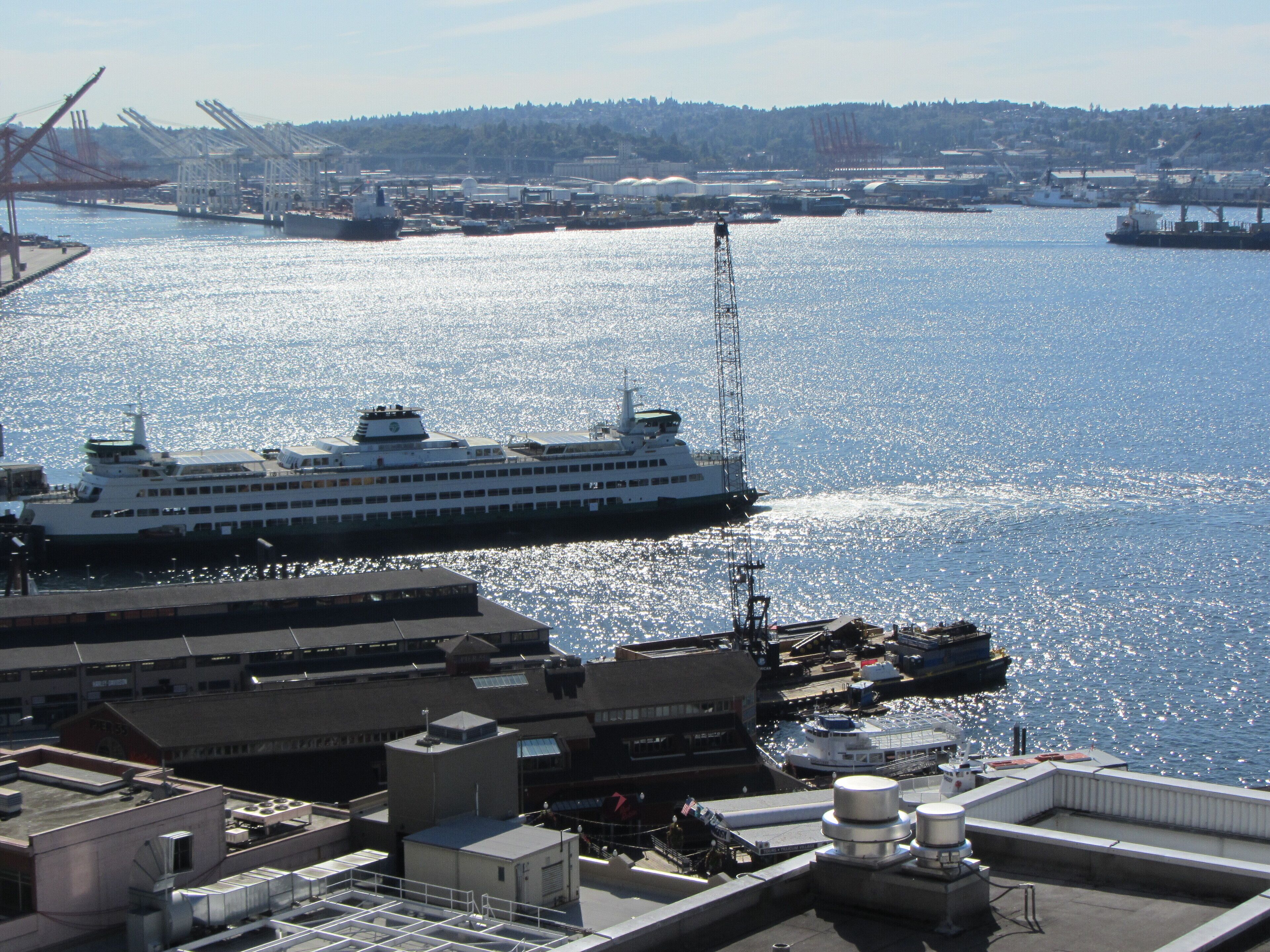 A large cruise ship docked at a port with industrial buildings and cranes in the background.