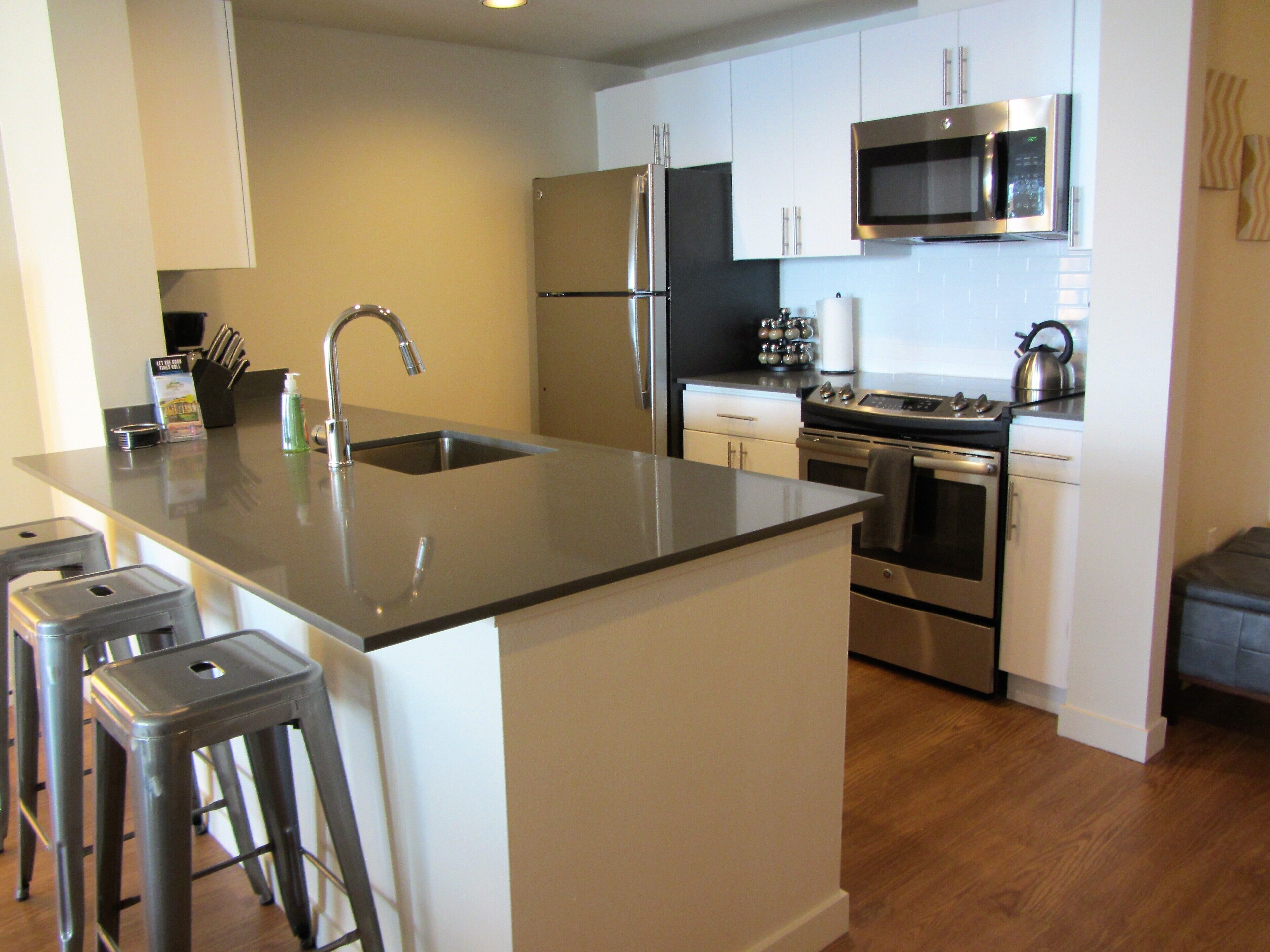A modern kitchen with stainless steel appliances, a central island with stools, and white cabinetry.