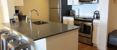 A modern kitchen with stainless steel appliances, a central island with stools, and white cabinetry.
