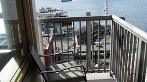 A balcony with a view of a waterfront, a chair, and a table.