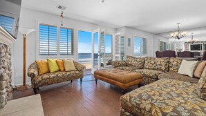 A spacious living room with a large sectional sofa, a stone accent wall, and a view of the ocean through open doors.
