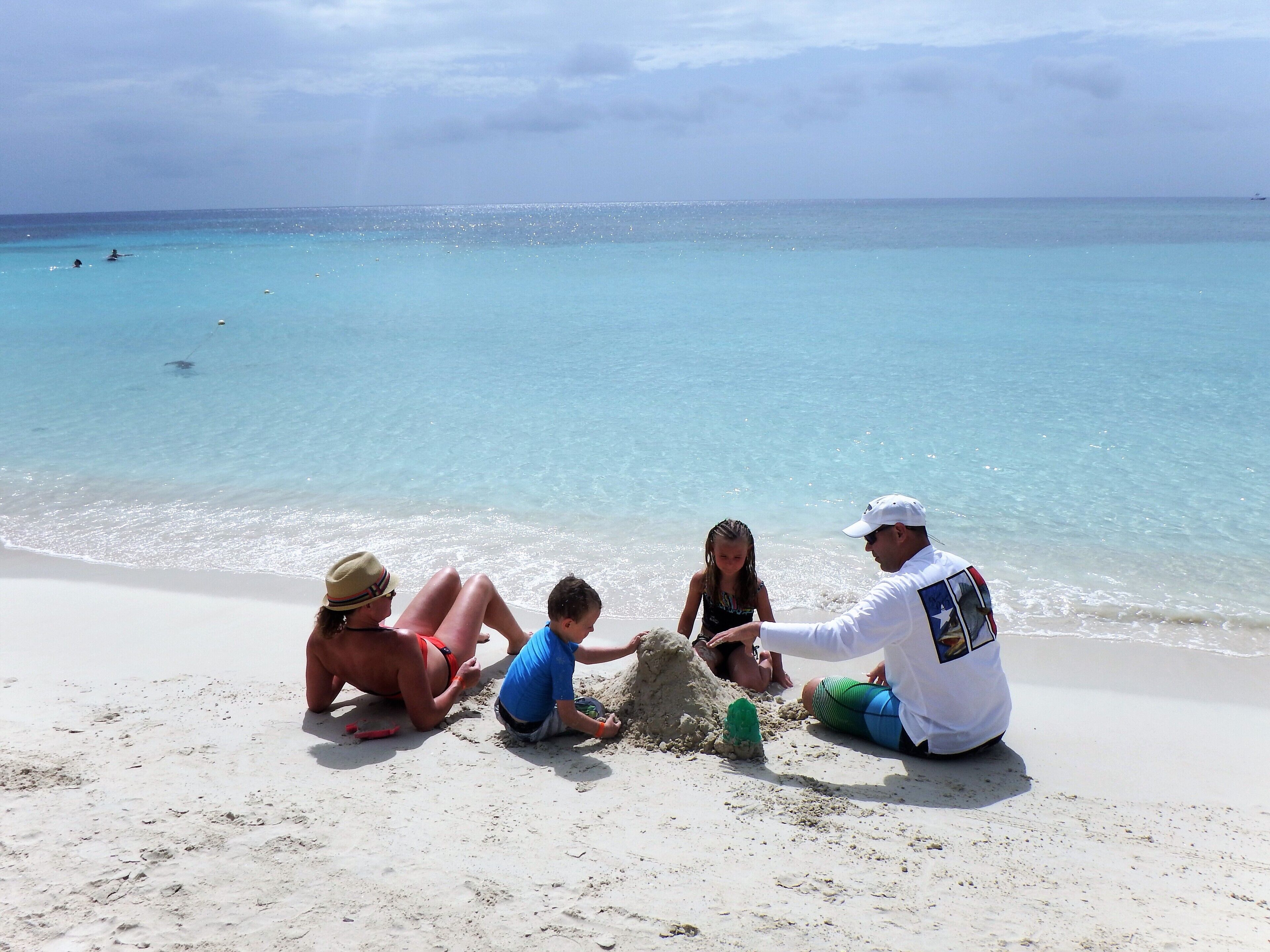 A beach scene with people sitting on the sand, a clear sky, and the ocean in the background.