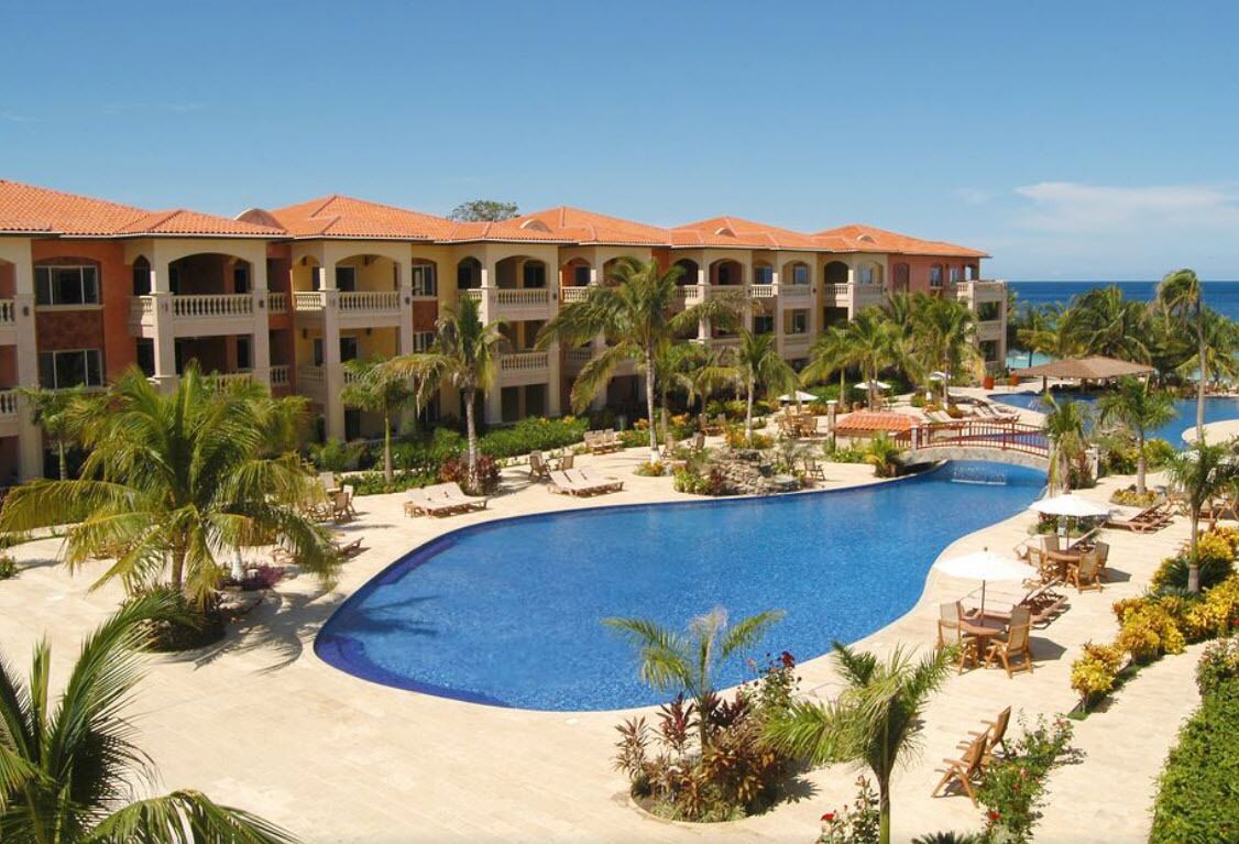 Ein Resort mit großem Pool, Palmen und einem Gebäude mit Balkonen.