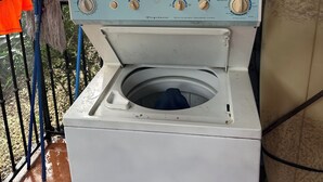 A front-loading washing machine with a front door, control panel, and a small window.