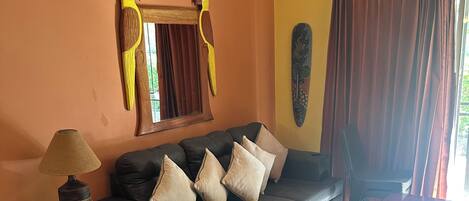 A living room with a sectional sofa, a small table, a lamp, and a wall-mounted air conditioner.