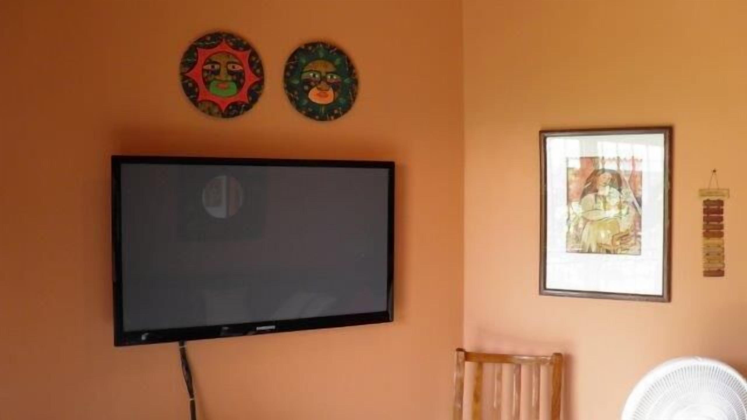 Une pièce dotée d’un téléviseur à écran plat fixé au mur, d’un tableau encadré et de deux masques décoratifs.