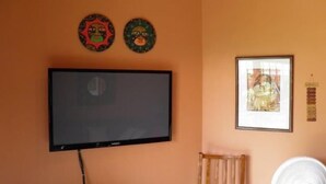 A room with a flat-screen TV mounted on the wall, a framed picture, and two decorative masks.