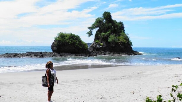 A beach with a person standing, rocky formations, and the ocean.