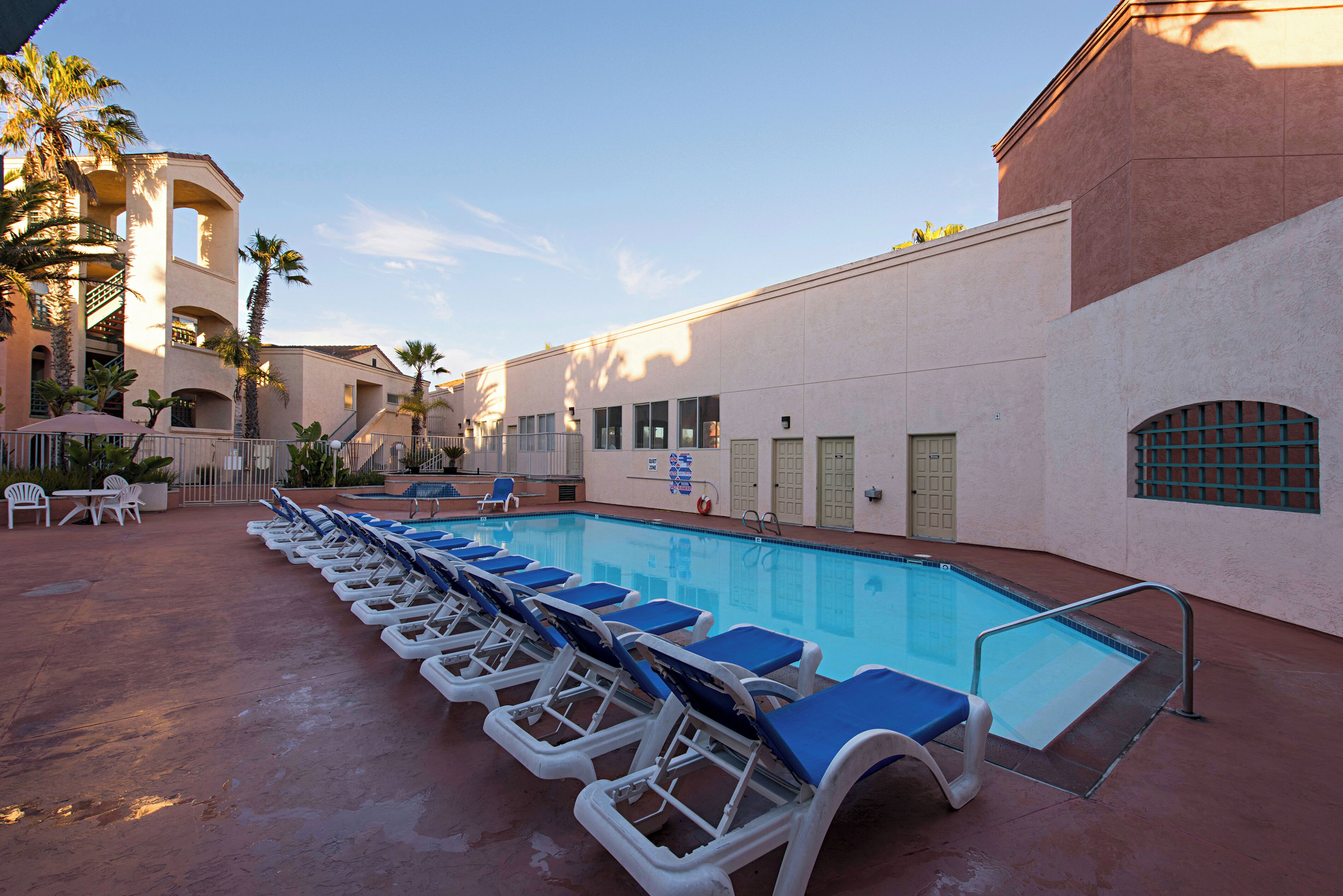 A swimming pool with lounge chairs, palm trees, and a building with a red wall and windows.