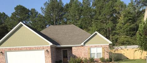 A two-story house with a brick facade, a green roof, and a white garage door.