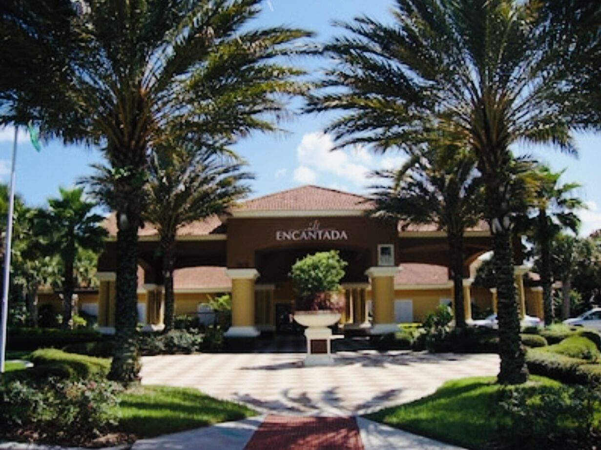 A hotel entrance with a sign reading "ENCANTADA," surrounded by palm trees and a well-maintained garden.