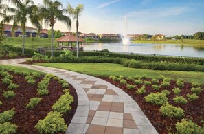A landscaped area with a paved walkway, a gazebo, and a body of water with a fountain. - Beautiful Spacious Townhome 5 miles to Disney Private Pool at Encantada Resort (Kissimmee)