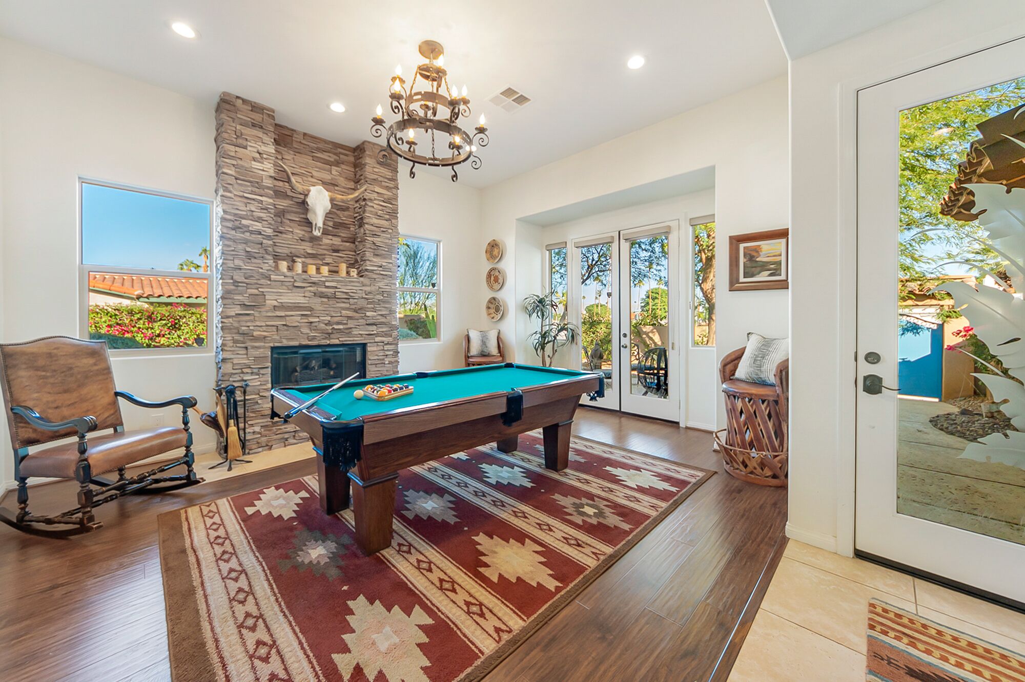 A pool room with a pool table, a stone fireplace, and a chandelier.
