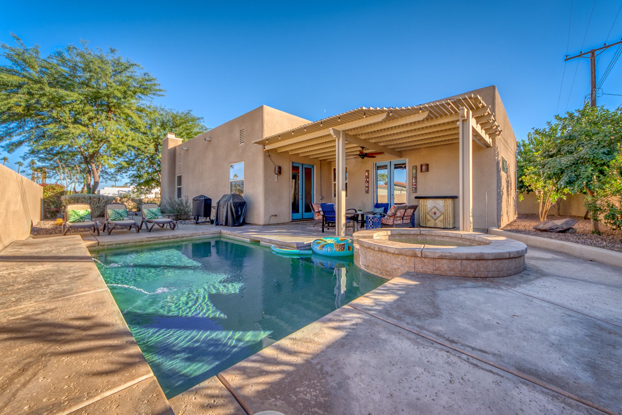 Une piscine dotée de chaises longues et d’un jacuzzi, entourée d’un patio aménagé avec du mobilier d’extérieur.