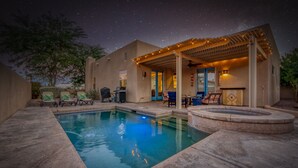 Una piscina con un porche cubierto, mobiliario exterior y un hogar de piedra.