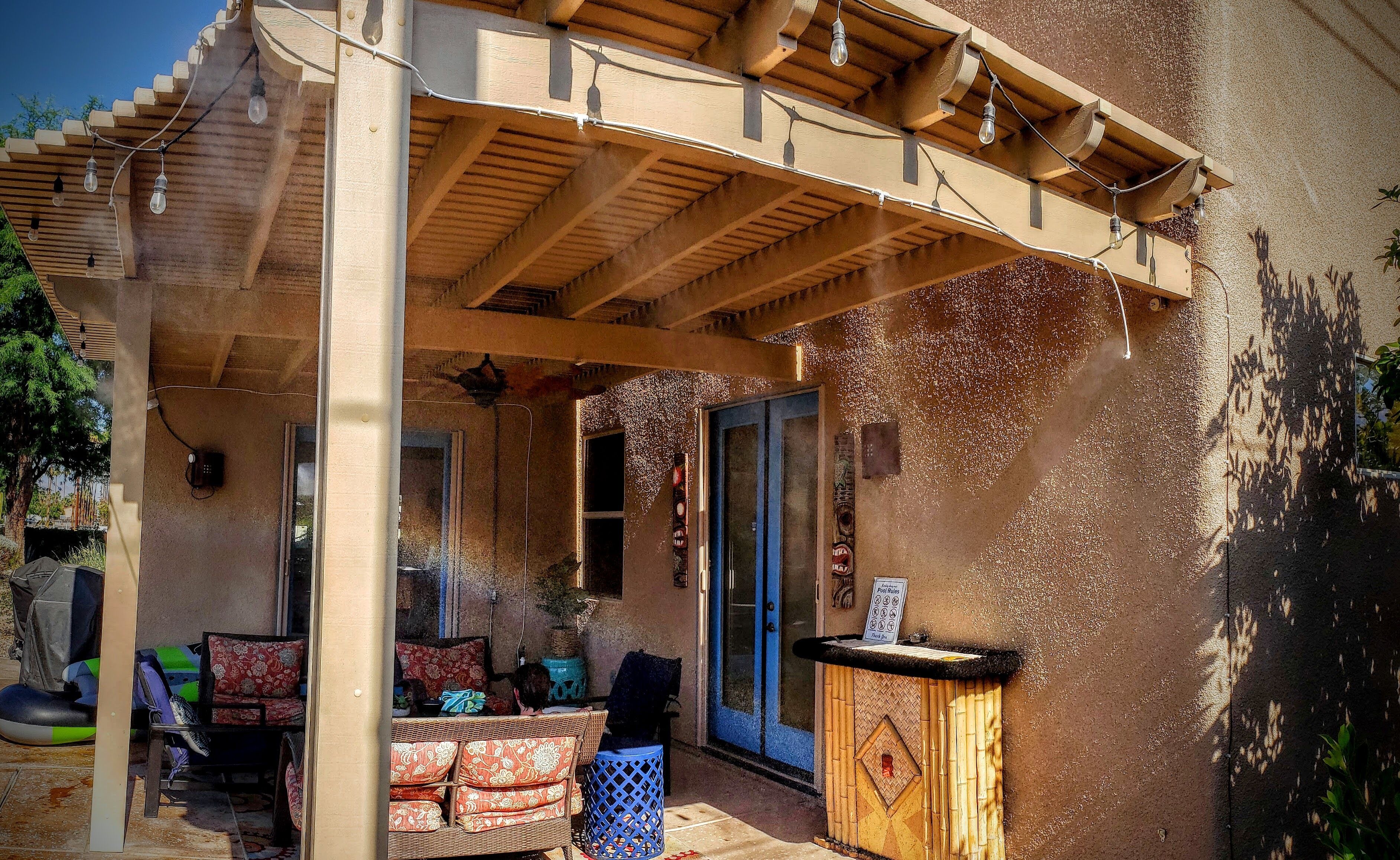 An outdoor patio with a wooden pergola, a table with chairs, and a small decorative cabinet.