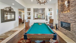 Una mesa de billar en una habitación luminosa con pared de piedra y chimenea.