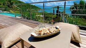A wooden deck with a table set for a meal, overlooking a pool and a scenic view of the ocean. - Luxury Waterfront Villa Pinel. Direct Ocean Views & Private Beach Access (SAINT MARTIN)