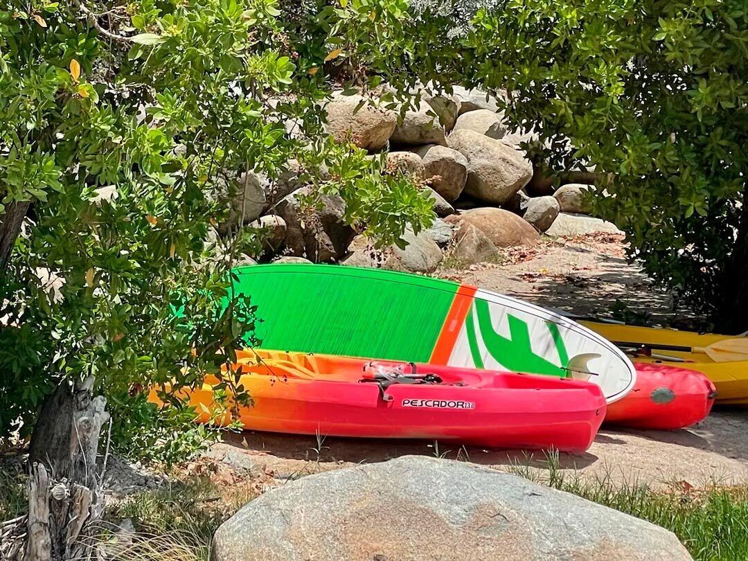 A red and green kayak with a white logo, resting on rocks near a body of water.
