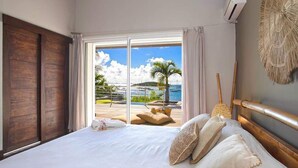 A bedroom with a large bed, a view of the sea, and a balcony with outdoor furniture. - Luxury Waterfront Villa Pinel. Direct Ocean Views & Private Beach Access (SAINT MARTIN)