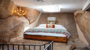 Ein Schlafzimmer mit einem hölzernen Bett, einer Chandelieber und einer Steinwand.