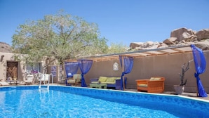 Ein Swimmingpool mit blauem Wasser, umgeben von Sitzgelegenheiten im Freien und einem überdachten Bereich mit blauen Vorhängen.