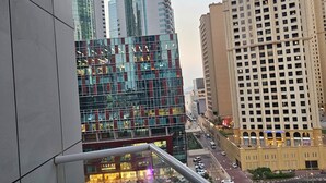 Un edificio moderno con fachada de vidrio, barandilla metálica y vista a un paisaje urbano con edificios altos.