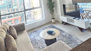 Una sala de estar moderna con un sofá, una mesa de centro, un mueble para TV y un amplio ventanal con vistas a la ciudad.