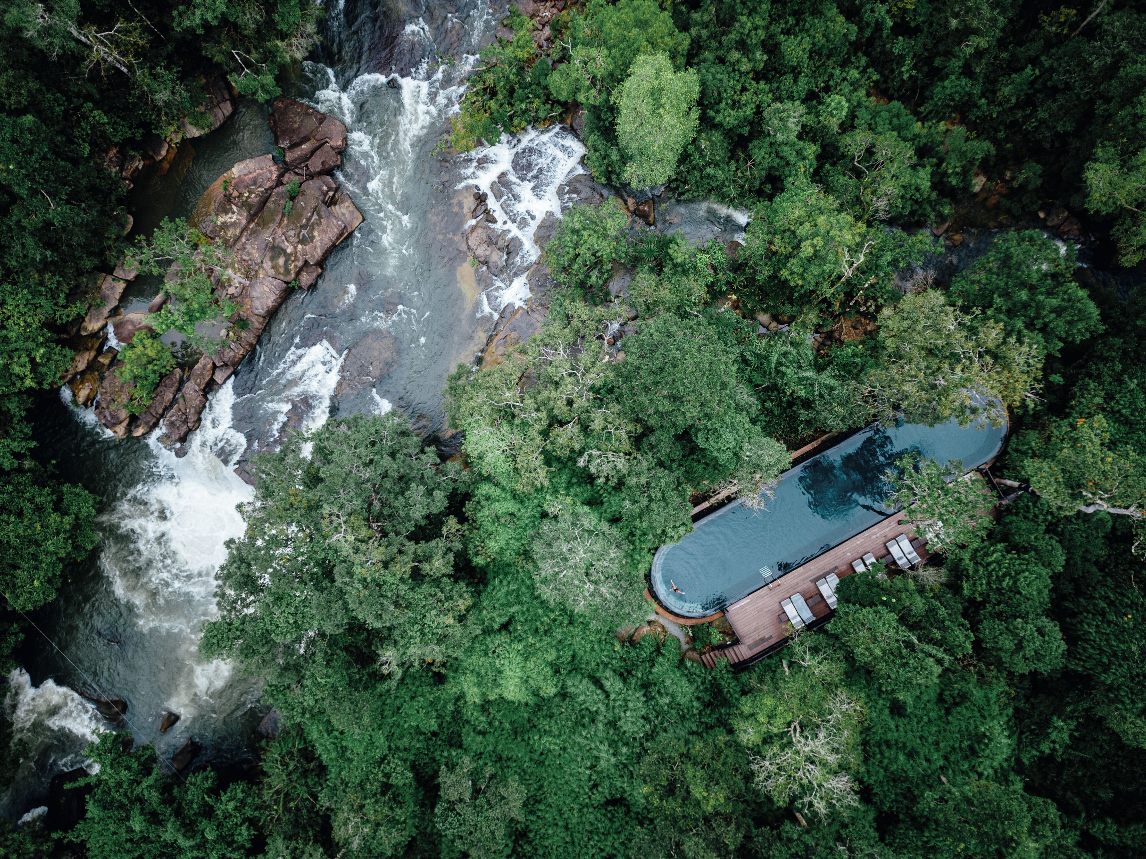 Vista aérea de un resort con piscina rodeada de bosque denso y una cascada.