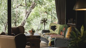 Une pièce confortable avec un canapé, un fauteuil, un ventilateur et une table sur laquelle se trouve un panier de fruits.