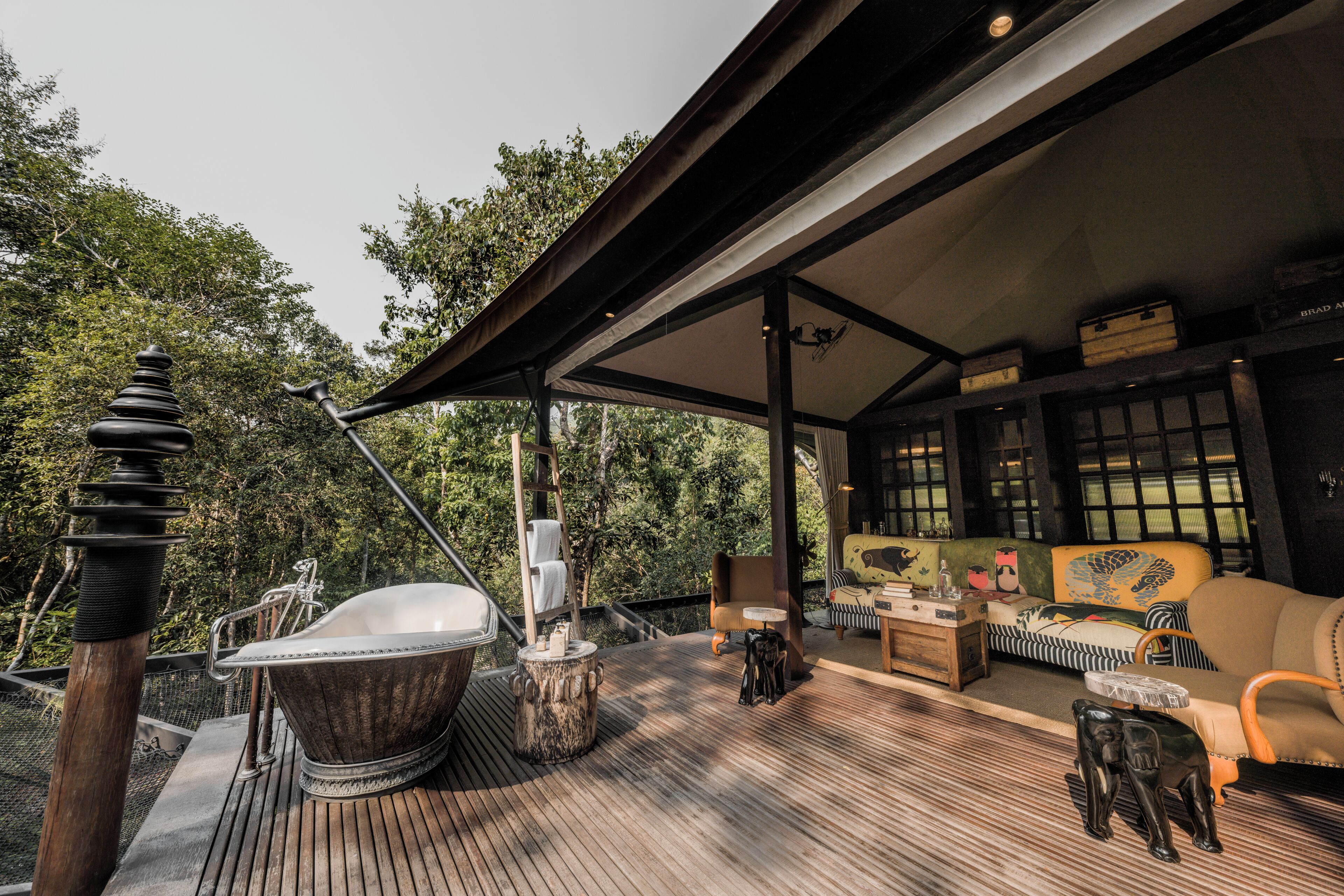 A wooden deck with a bathtub, lounge chairs, and a sofa.