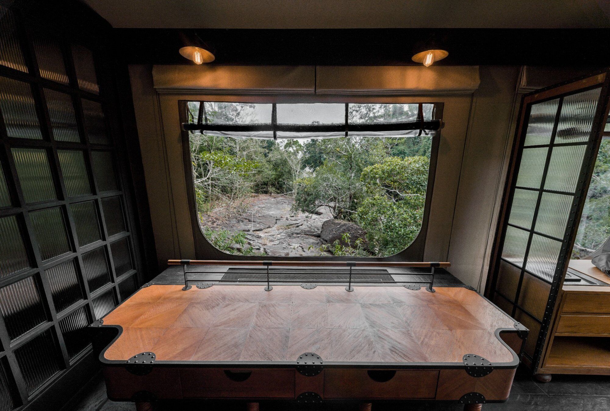 A room with a large window, a wooden table, and a view of a rocky outdoor area.