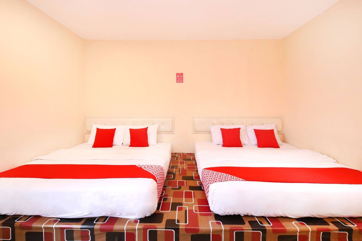 A hotel room with two beds, each with white bedding and red accents, and a patterned carpet.