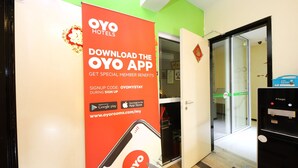 Interior de un hotel con un cartel promocional de la aplicación OYO, una puerta de vidrio de entrada y un refrigerador Magic negro.