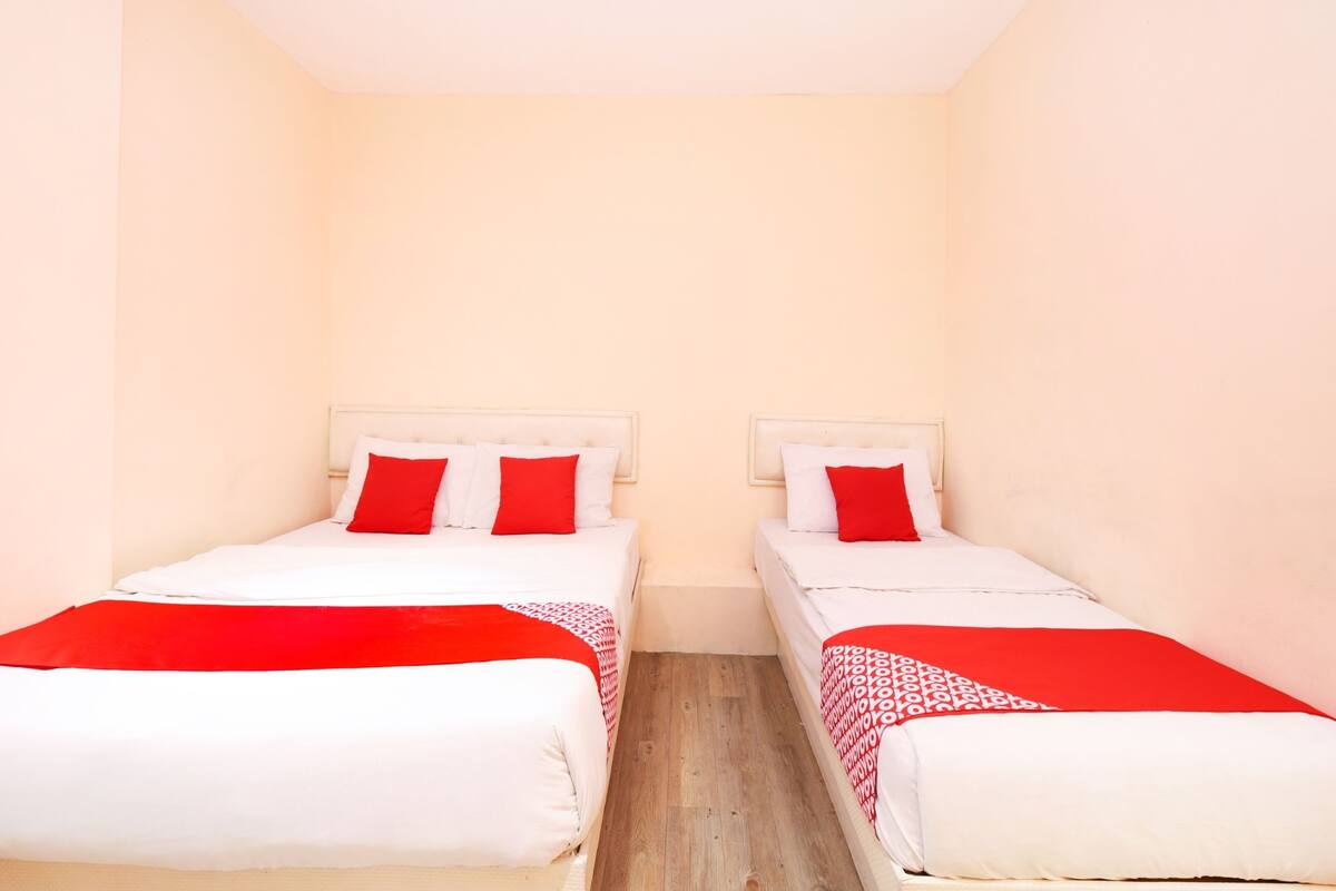 A small, single-room hotel room with two beds, each with white bedding and red accents.
