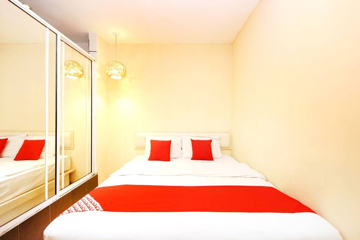A hotel room with a bed, a mirror, and a red and white bedspread.