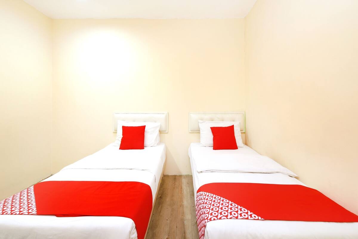 A room with two beds, each with a white headboard and red pillows.