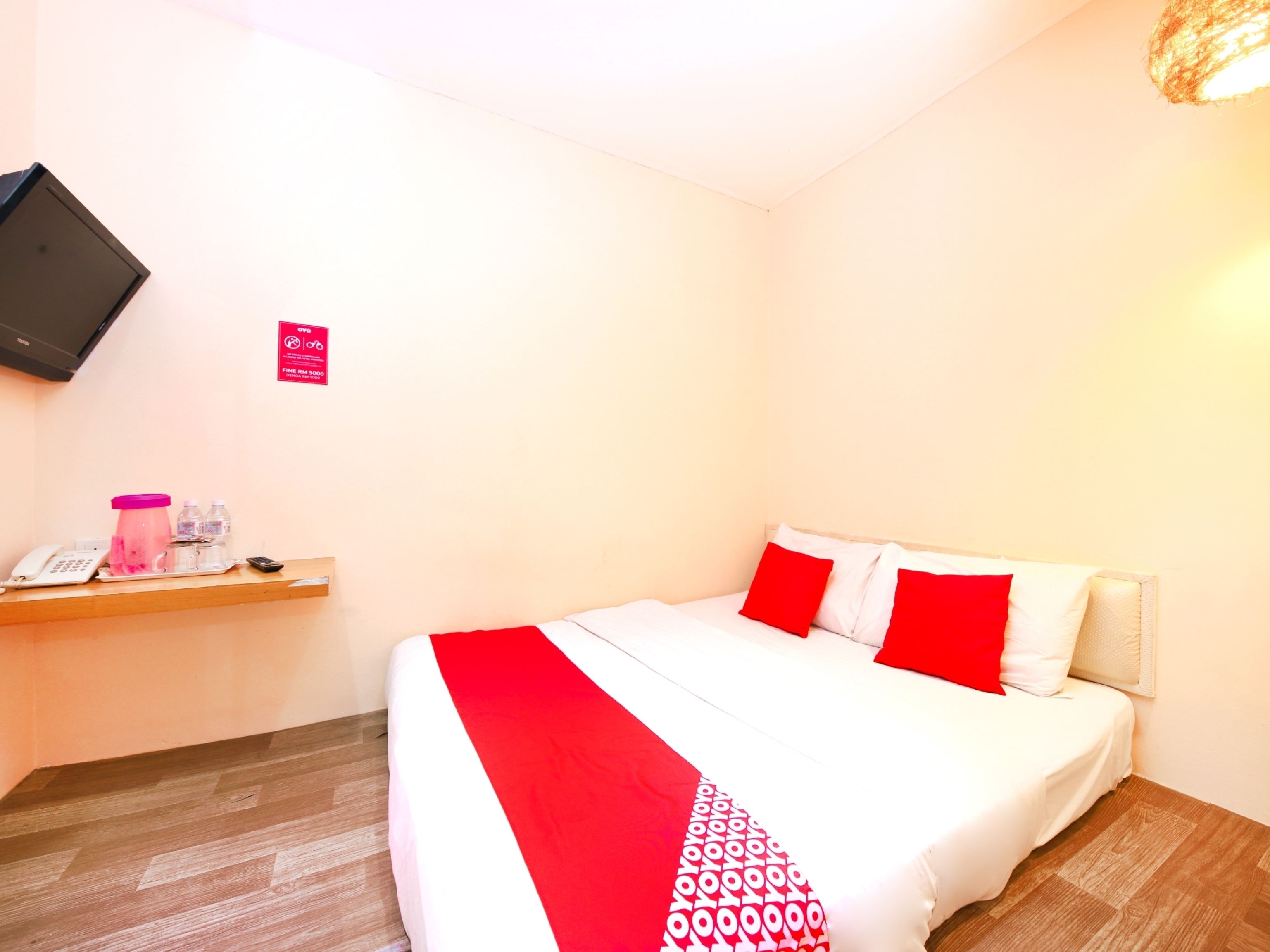 Hotelkamer met een bed, nachtkastje met telefoon, waterdispenser en een aan de muur bevestigde televisie.