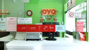 Un mostrador de recepción de hotel con una pared verde, un reloj y un letrero que indica la entrada a las 2 PM y la salida a las 12 PM.