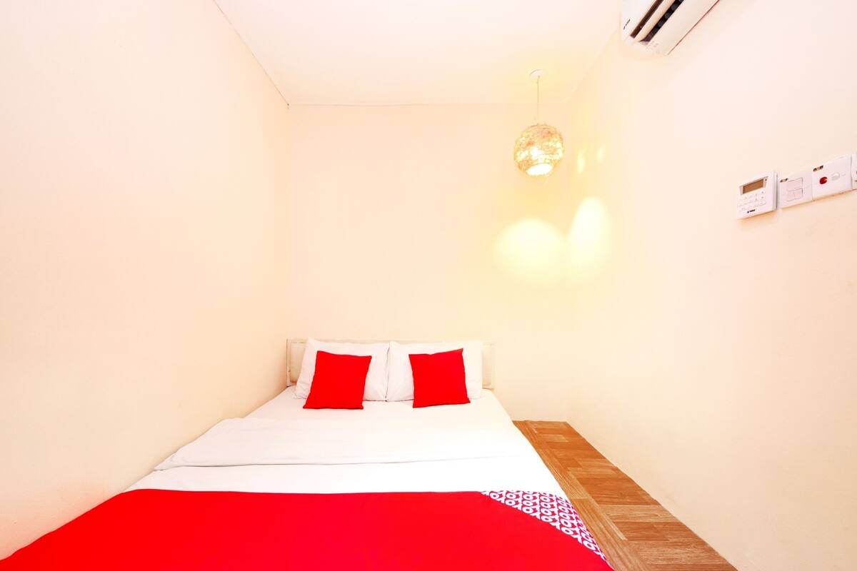 A bedroom with a bed, white walls, a wooden floor, and a hanging light fixture.