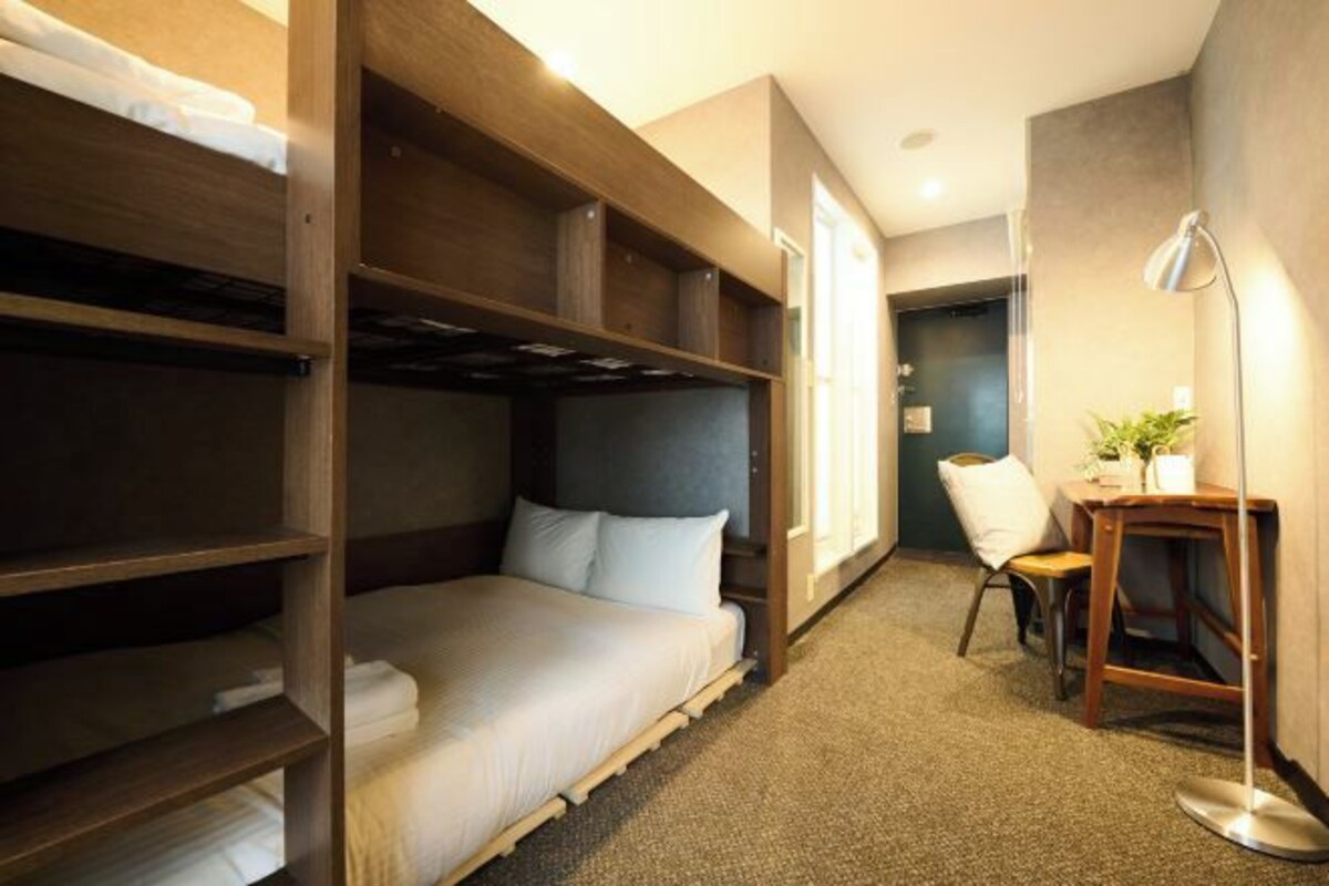 A hotel room with bunk beds, a desk, a chair, and a floor lamp.