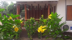 A building with a tiled roof and a covered porch. There are yellow flowers in the foreground. - Ramidahost2 (Chiang Saen)