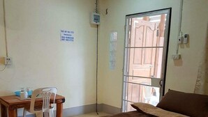 A bedroom with a brown bedspread, two rolled towels, a wooden desk with a chair, a small trash bin, and a door leading outside. - Ramidahost2 (Chiang Saen)