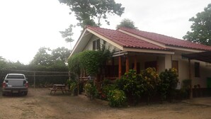 A house with a red tiled roof, a porch with wooden pillars, and a gravel driveway. - Ramidahost2 (Chiang Saen)