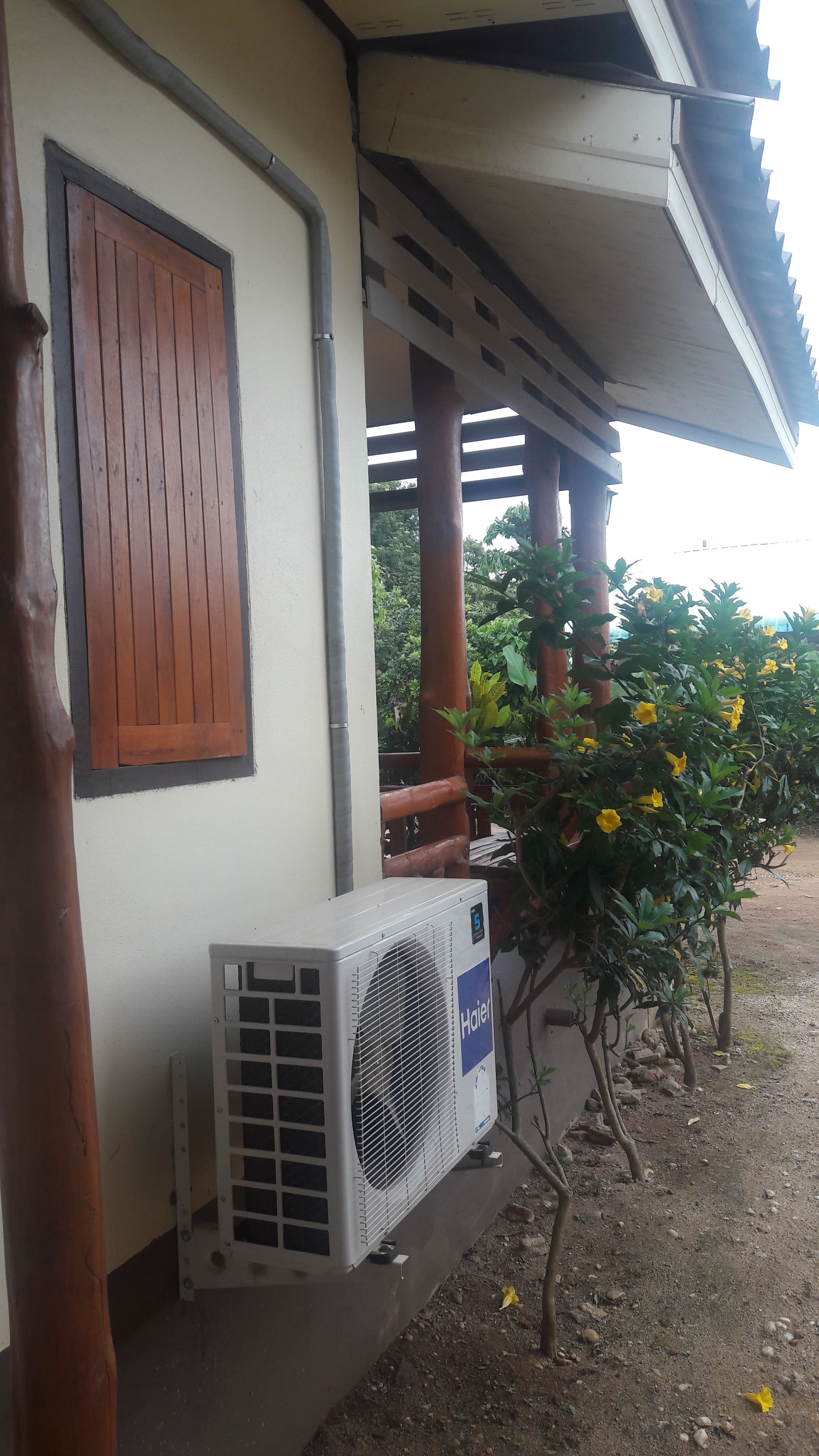 An air conditioning unit outside a building with a wooden door and a metal frame.